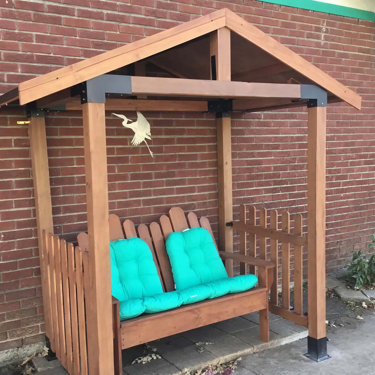 Angled view of a shaded seating area built with a 4x4 four-post pergola bracket kit, featuring a wooden bench with turquoise cushions.