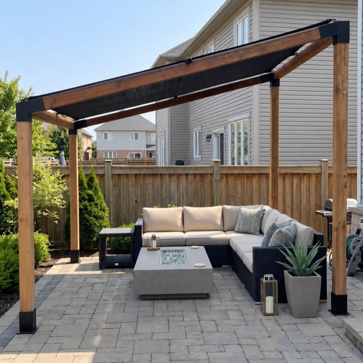 Front view of a pergola built with a sloped-roof bracket kit, with a black shade canopy over a cream sectional sofa and fire pit table.